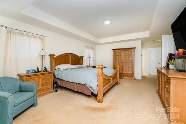 bedroom with a raised ceiling and light colored carpet