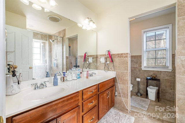 bathroom featuring tile patterned flooring, tiled shower, toilet, vanity, and tile walls