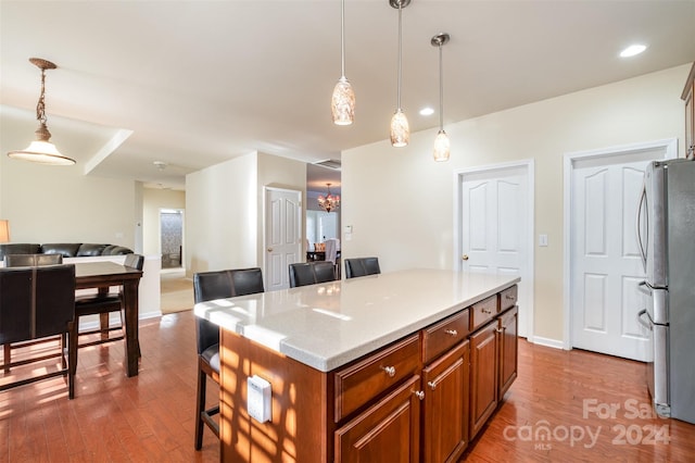 kitchen featuring stainless steel fridge, decorative light fixtures, a kitchen island, and wood-type flooring