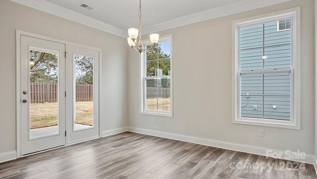 unfurnished dining area with hardwood / wood-style flooring, crown molding, and an inviting chandelier