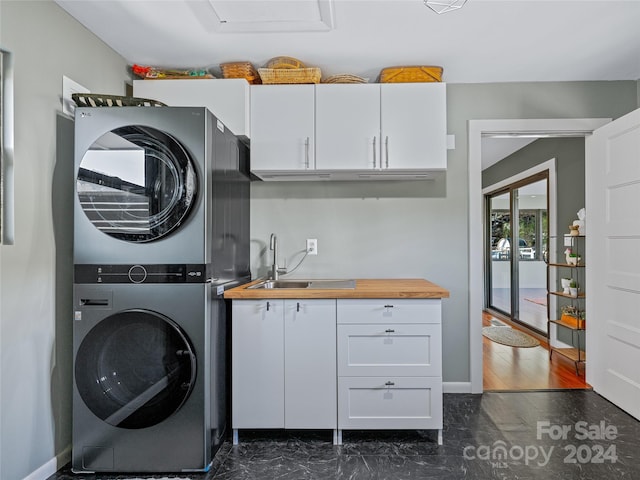 laundry room featuring cabinets, stacked washing maching and dryer, sink, and dark wood-type flooring