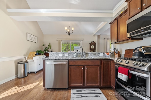 kitchen with light stone countertops, stainless steel appliances, sink, wood-type flooring, and a notable chandelier