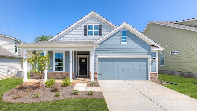 craftsman-style home with covered porch, a garage, central air condition unit, and a front yard