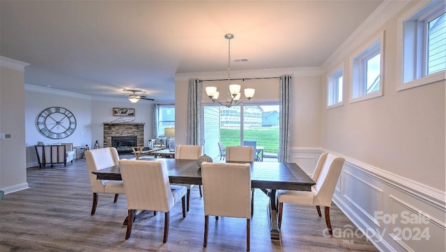 dining room with a stone fireplace, ornamental molding, dark hardwood / wood-style floors, and ceiling fan with notable chandelier