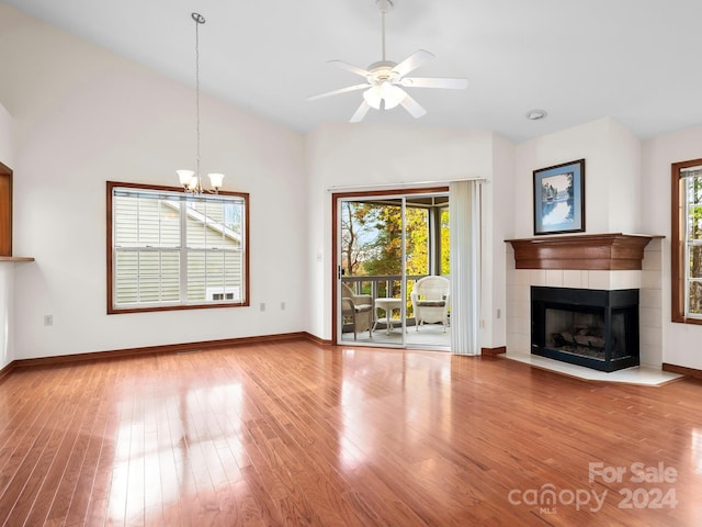 unfurnished living room featuring hardwood / wood-style floors, a tiled fireplace, lofted ceiling, and ceiling fan with notable chandelier