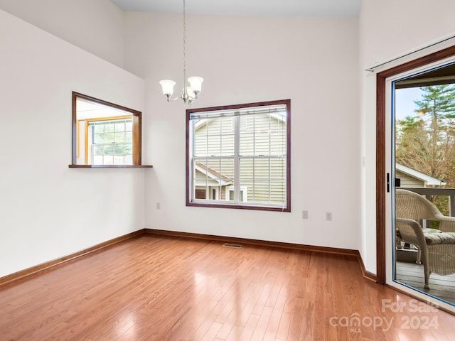 unfurnished room with hardwood / wood-style floors, a notable chandelier, and a high ceiling