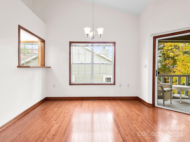 unfurnished room featuring hardwood / wood-style floors, plenty of natural light, lofted ceiling, and a notable chandelier