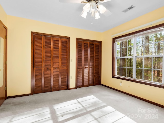 unfurnished bedroom with ceiling fan, light carpet, and two closets