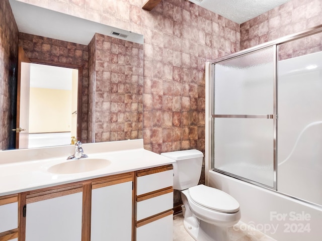 full bathroom with tile patterned floors, vanity, a textured ceiling, toilet, and combined bath / shower with glass door