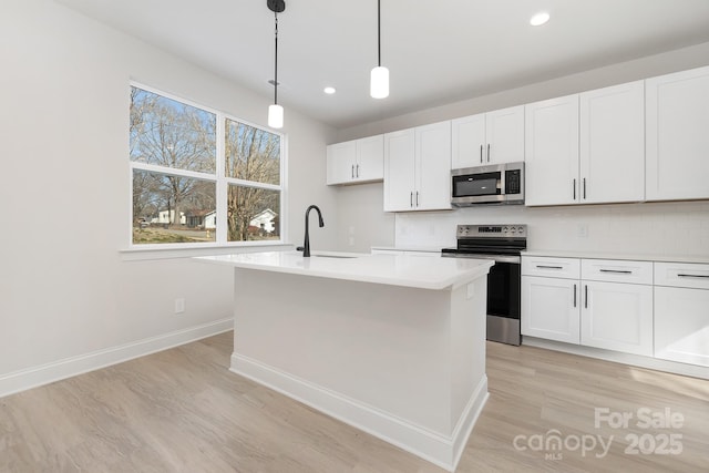 kitchen with pendant lighting, light countertops, appliances with stainless steel finishes, a sink, and an island with sink