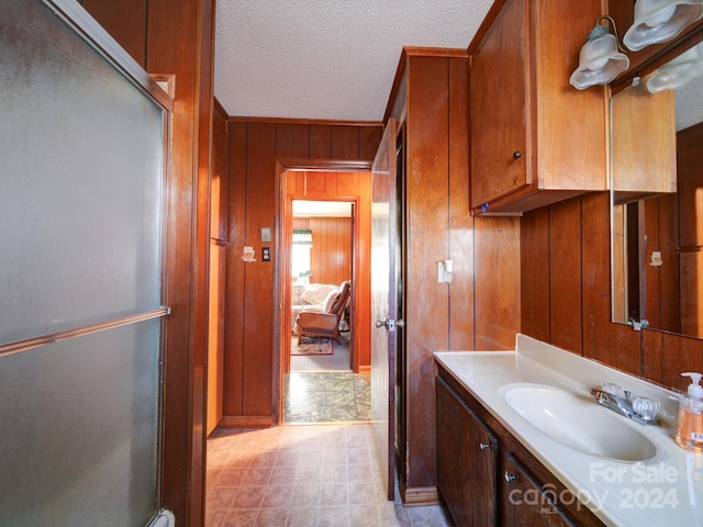 bathroom with a textured ceiling, vanity, an enclosed shower, and wooden walls