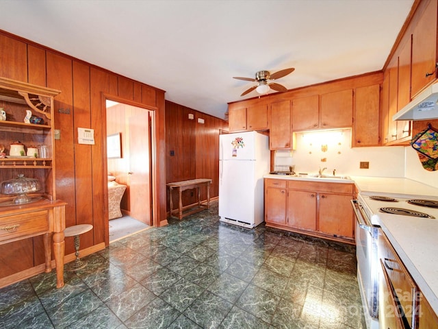 kitchen featuring white appliances, ceiling fan, wooden walls, and sink