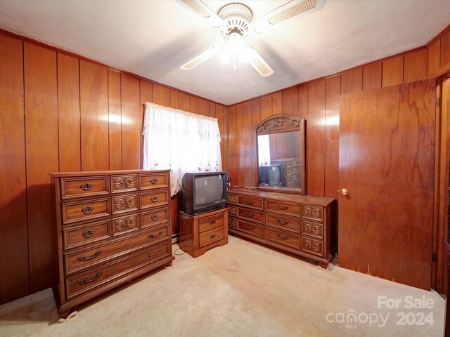 carpeted bedroom featuring ceiling fan and wood walls