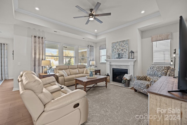 living room featuring a premium fireplace, light hardwood / wood-style flooring, ceiling fan, and a tray ceiling