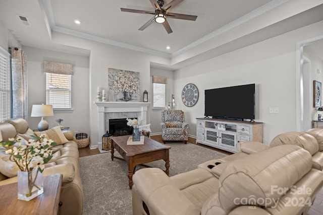 living room featuring wood-type flooring, ceiling fan, crown molding, a tray ceiling, and a fireplace