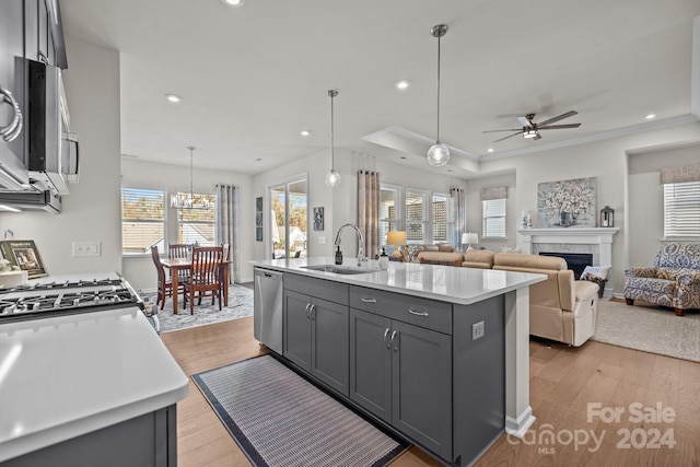 kitchen featuring a center island with sink, decorative light fixtures, gray cabinets, sink, and light hardwood / wood-style flooring