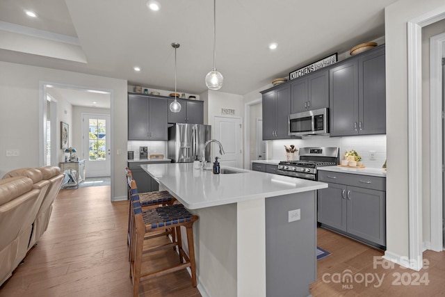 kitchen with stainless steel appliances, hardwood / wood-style floors, an island with sink, a breakfast bar, and pendant lighting