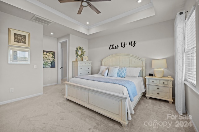 carpeted bedroom featuring ceiling fan, multiple windows, and a raised ceiling