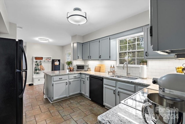 kitchen featuring light stone countertops, sink, black appliances, and kitchen peninsula