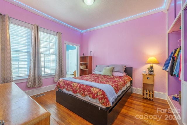 bedroom with wood-type flooring, ornamental molding, and multiple windows