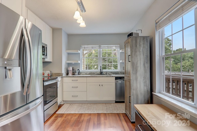 kitchen featuring white cabinetry, sink, appliances with stainless steel finishes, light wood-type flooring, and pendant lighting