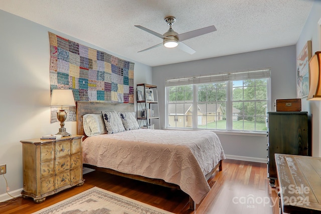 bedroom with hardwood / wood-style floors, ceiling fan, and a textured ceiling