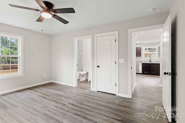 unfurnished bedroom with ensuite bath, light hardwood / wood-style flooring, multiple windows, and ceiling fan