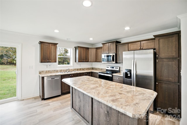 kitchen with light hardwood / wood-style floors, appliances with stainless steel finishes, light stone countertops, a kitchen island, and crown molding