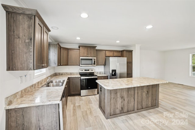 kitchen with stainless steel appliances, sink, ornamental molding, a center island, and light wood-type flooring