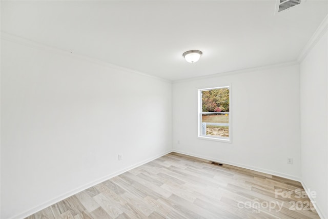 spare room with light wood-type flooring, baseboards, visible vents, and ornamental molding