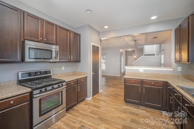 kitchen featuring stainless steel appliances, an inviting chandelier, kitchen peninsula, pendant lighting, and light wood-type flooring