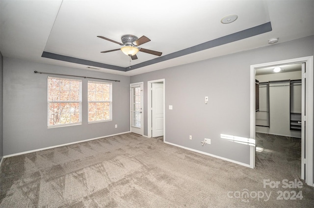 unfurnished bedroom with a tray ceiling, a walk in closet, ceiling fan, and carpet