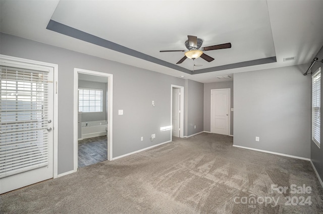 unfurnished bedroom with carpet flooring, ceiling fan, connected bathroom, and a tray ceiling