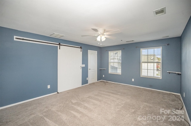 carpeted empty room with a barn door and ceiling fan