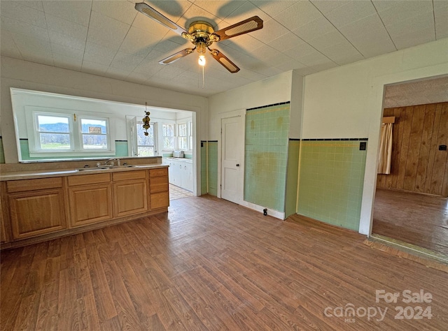 kitchen featuring light hardwood / wood-style floors, wooden walls, sink, ceiling fan, and pendant lighting