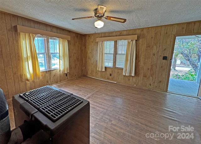 interior space featuring ceiling fan, wood-type flooring, wooden walls, and a textured ceiling