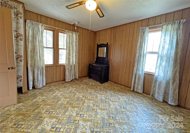 interior space featuring a wealth of natural light, wooden walls, and ceiling fan