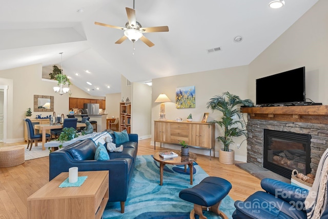 living room with a stone fireplace, light wood-type flooring, lofted ceiling, and ceiling fan with notable chandelier