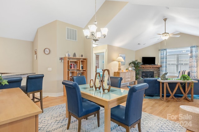 dining room featuring a fireplace, ceiling fan with notable chandelier, light wood-type flooring, and lofted ceiling