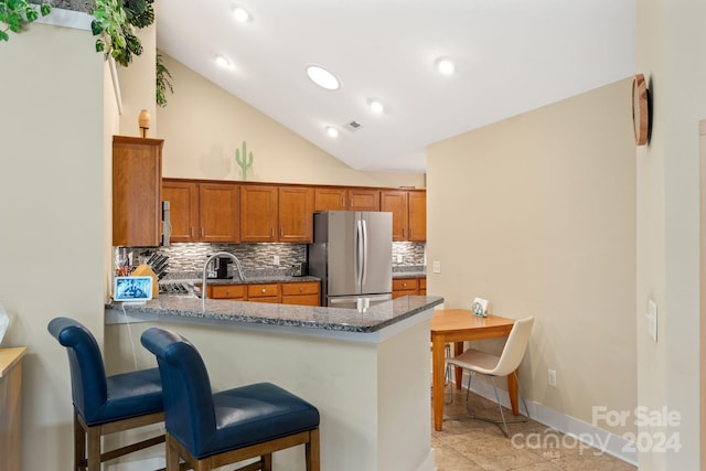 kitchen featuring light tile patterned flooring, kitchen peninsula, dark stone counters, lofted ceiling, and stainless steel fridge