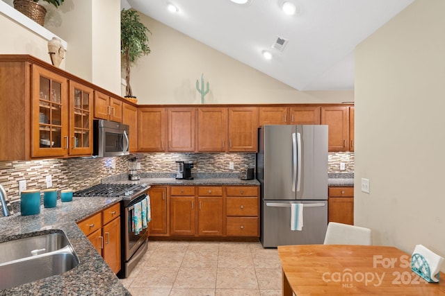 kitchen featuring stainless steel appliances, dark stone counters, decorative backsplash, sink, and high vaulted ceiling