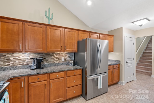 kitchen featuring lofted ceiling, dark stone counters, decorative backsplash, light tile patterned floors, and stainless steel fridge