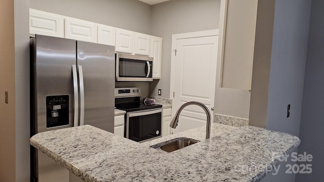 kitchen featuring appliances with stainless steel finishes, white cabinetry, sink, light stone counters, and kitchen peninsula