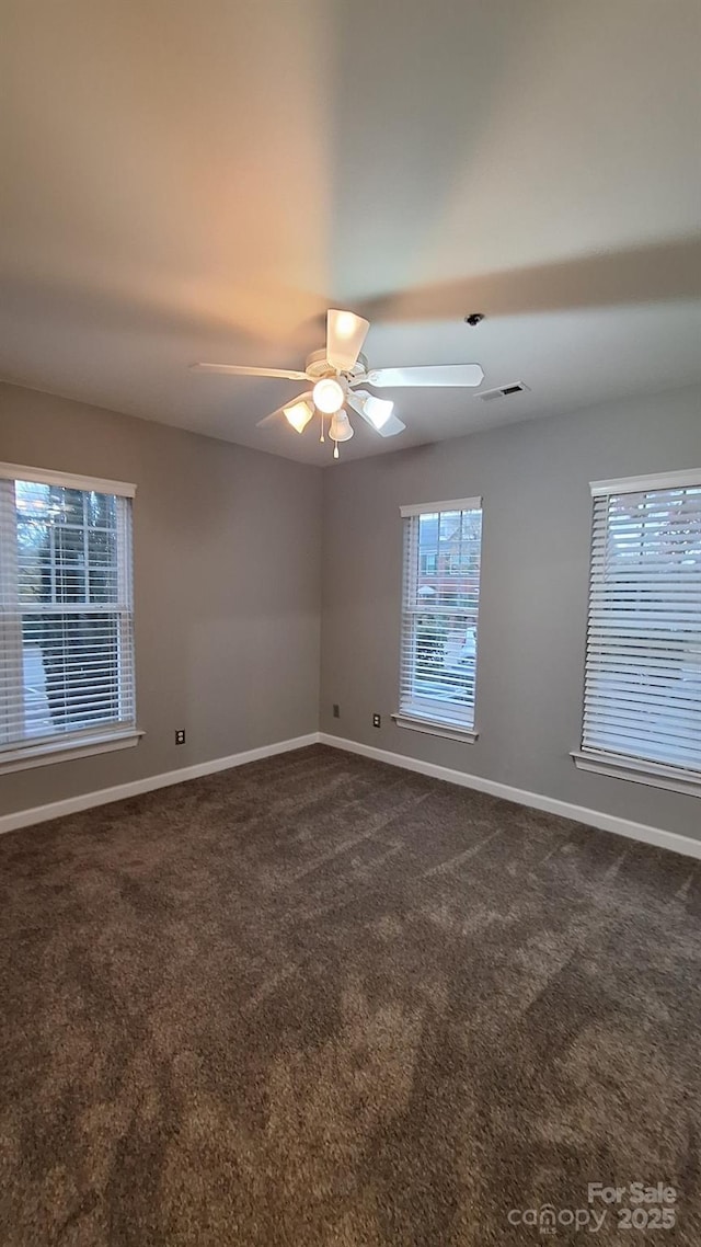 empty room with ceiling fan and dark colored carpet