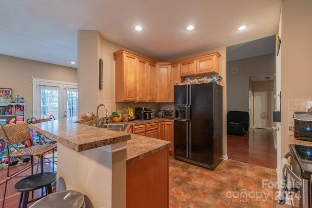 kitchen featuring black fridge, sink, electric range, kitchen peninsula, and a breakfast bar area