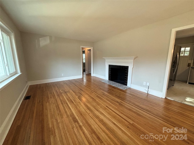 unfurnished living room featuring wood-type flooring and a tiled fireplace