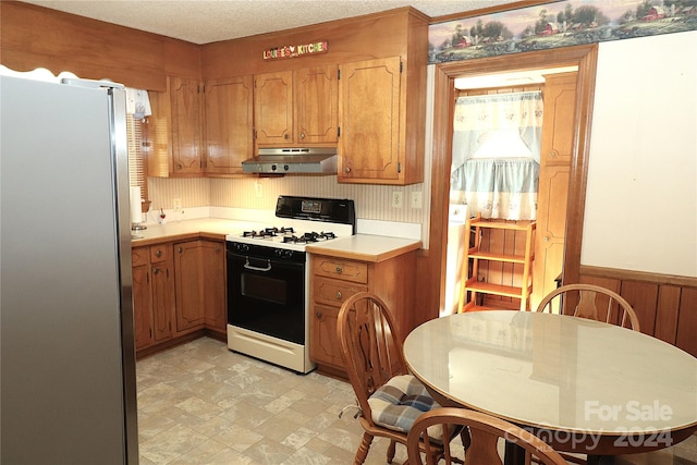 kitchen with stainless steel fridge, a textured ceiling, wooden walls, and white range with gas stovetop