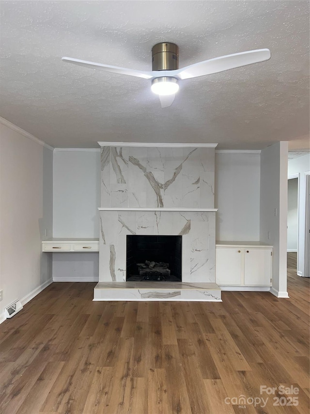 unfurnished living room with a textured ceiling, visible vents, a high end fireplace, baseboards, and ornamental molding