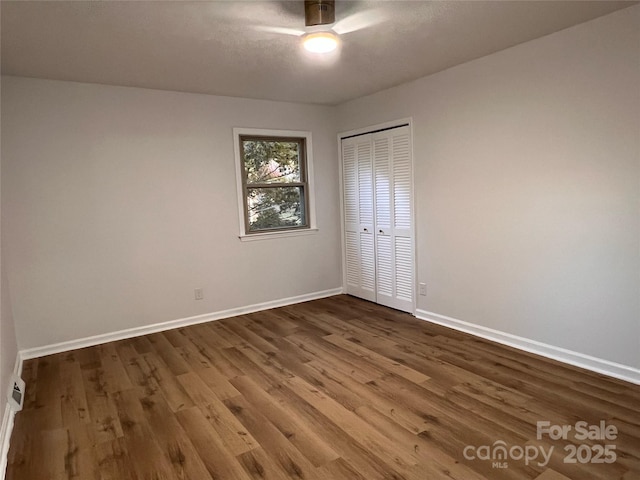 unfurnished bedroom with a ceiling fan, baseboards, dark wood finished floors, and a closet