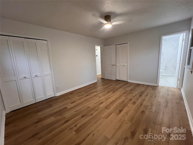 unfurnished bedroom featuring baseboards, connected bathroom, multiple closets, and wood finished floors
